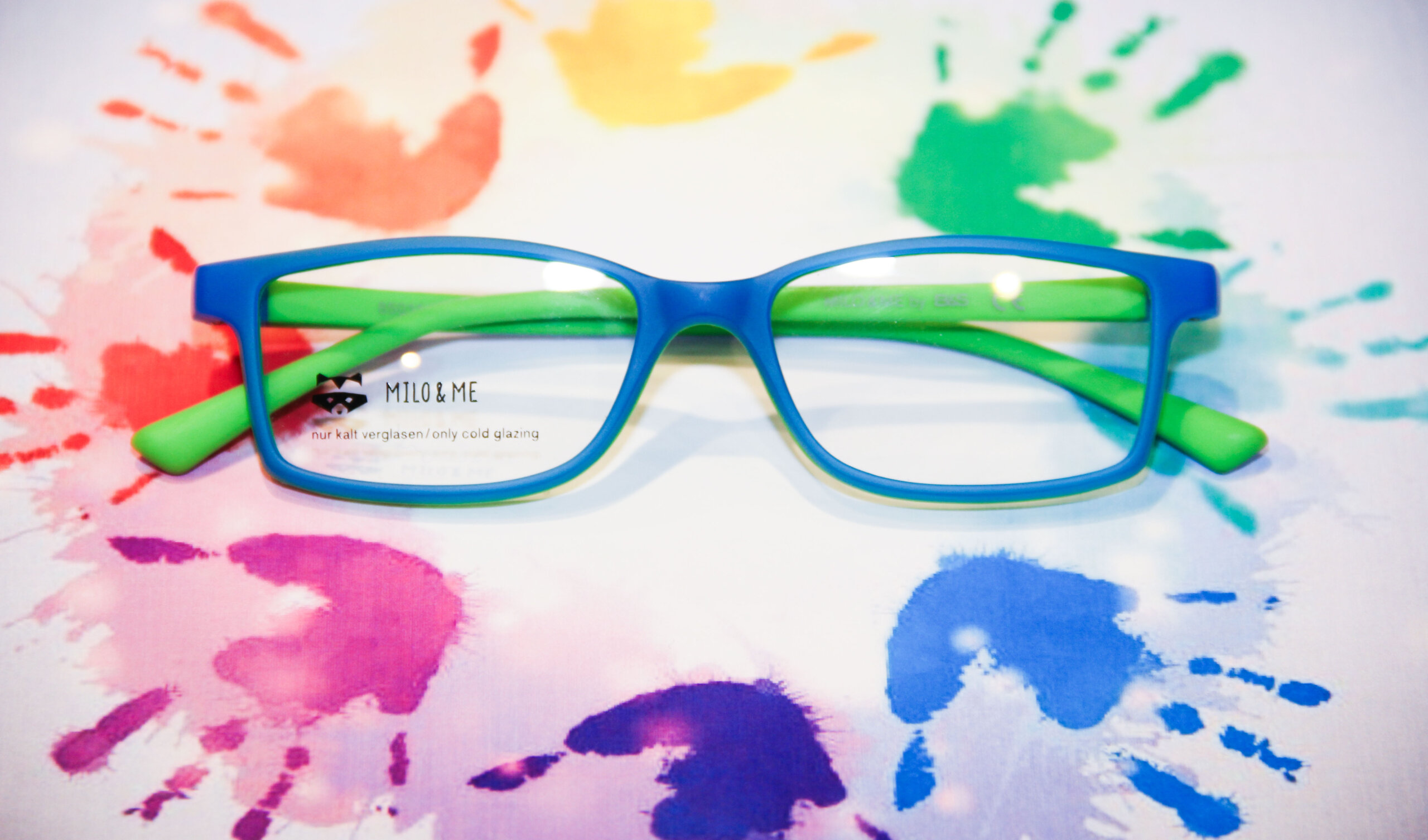 baer_optik_bremgarten_brille_06_web Detailansicht einer Kinderbrille mit grün-blauem Rahmen auf kreativem Untergrund