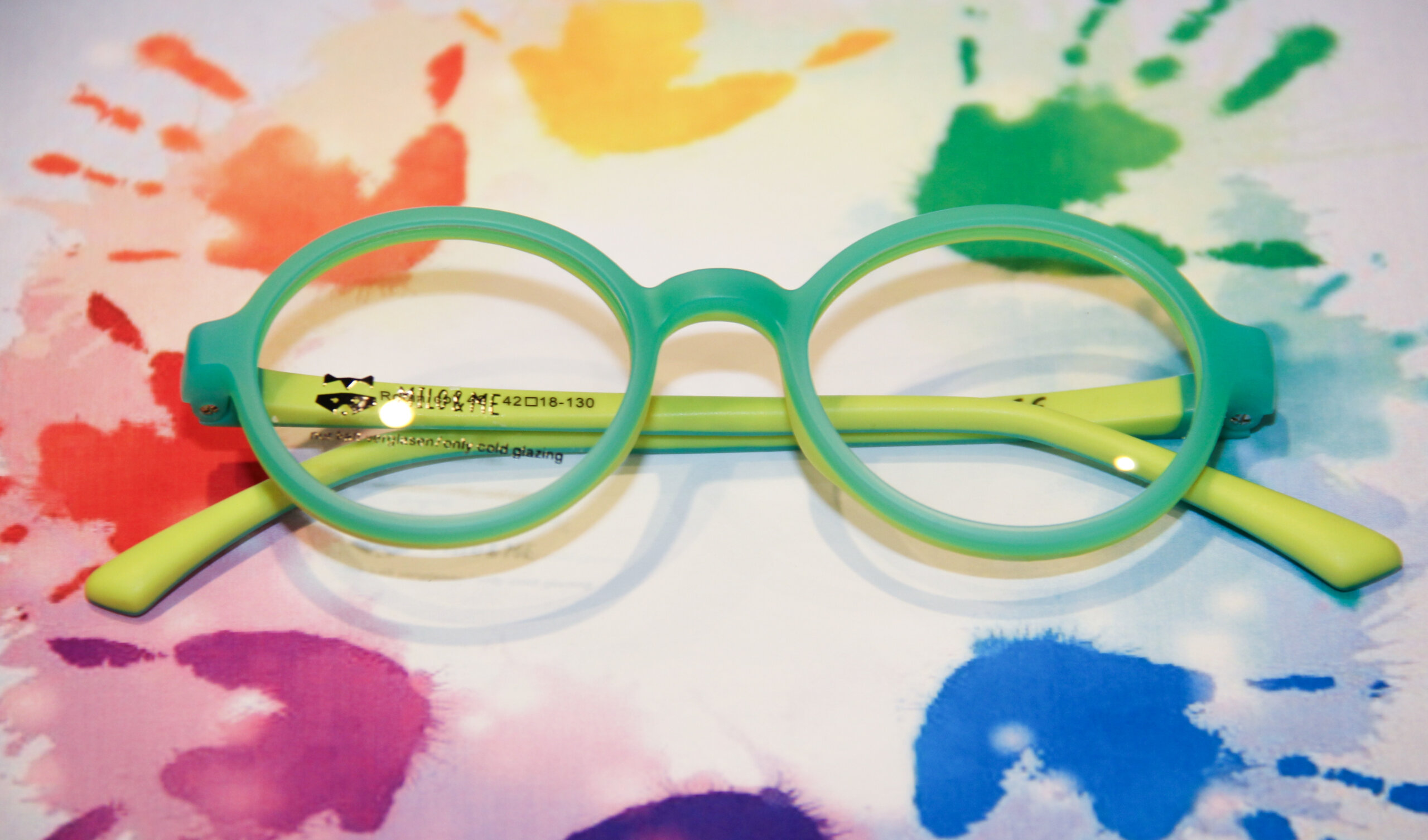 baer_optik_bremgarten_brille_23_web Farbenfrohe Kinderbrille vor Hintergrund mit bunten Handabdrücken